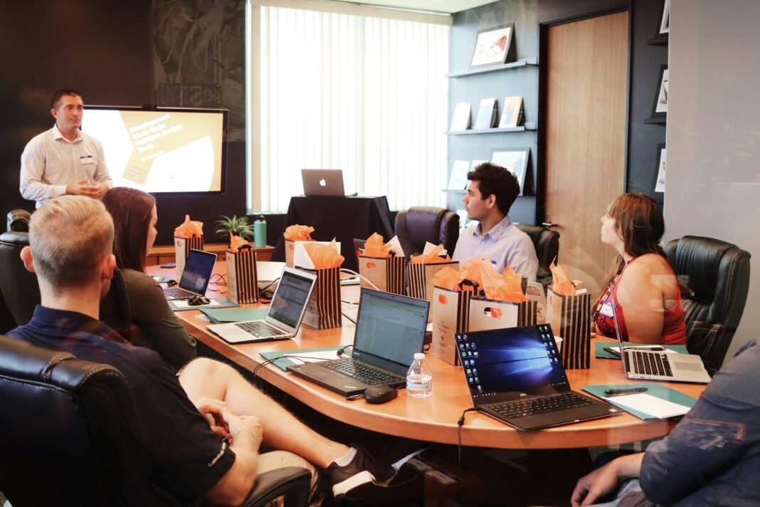 What Makes a Good Leader? 7 Qualities Backed by Research Leader standing and speaking to a team seated around a meeting table