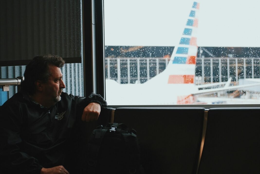 Man sitting in an airport lounge watching a plane through the window, thinking about relocating abroad