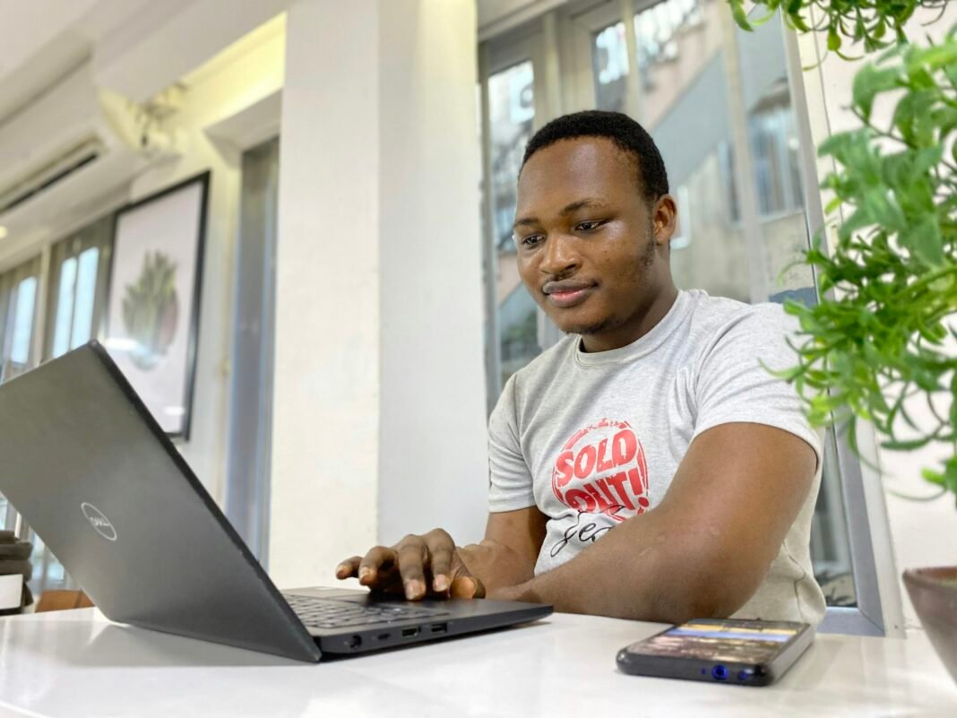 AI Is Changing Work: Here’s How Nigerians Can Stay Valuable Young Nigerian man smiling while working on a laptop, building AI skills