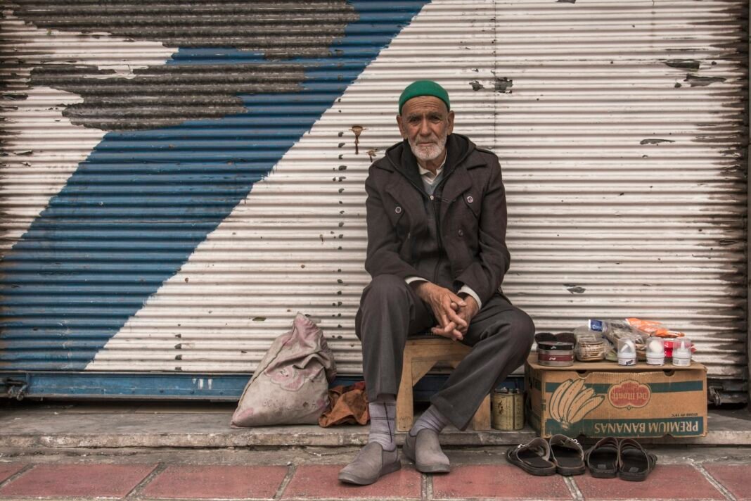 Man sitting alone on a bench in front of closed shop shutters, reflecting after a business setback