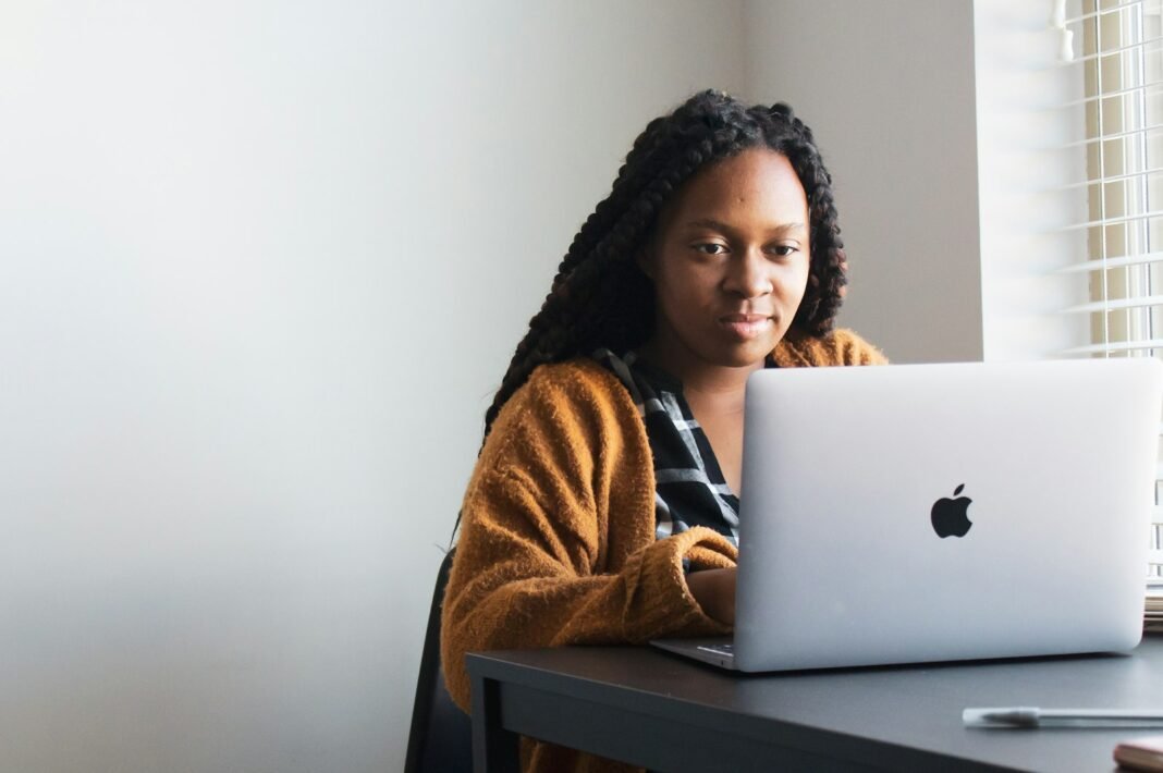 Young African woman with braids working on a laptop at a desk, representing remote jobs in Nigeria