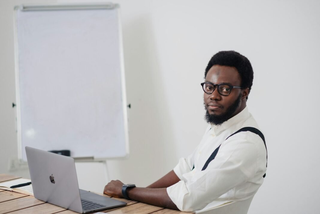 Young Nigerian man sitting at a table working on a laptop, reviewing tasks set up with AI tools