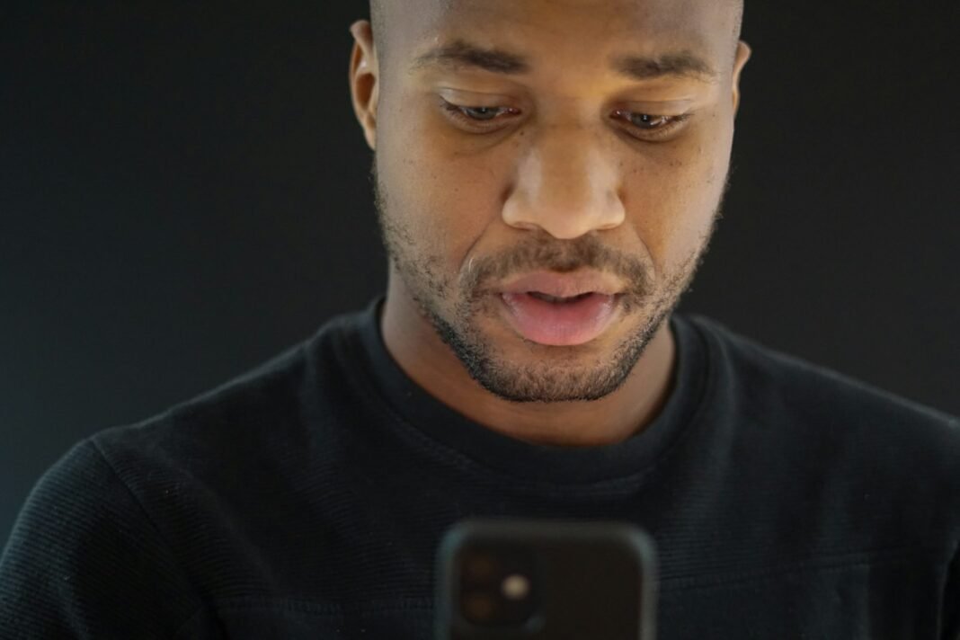Before You Send Your CV, Check These Fake Job Offer Signs Young Black man reading a message on his phone with a serious expression
