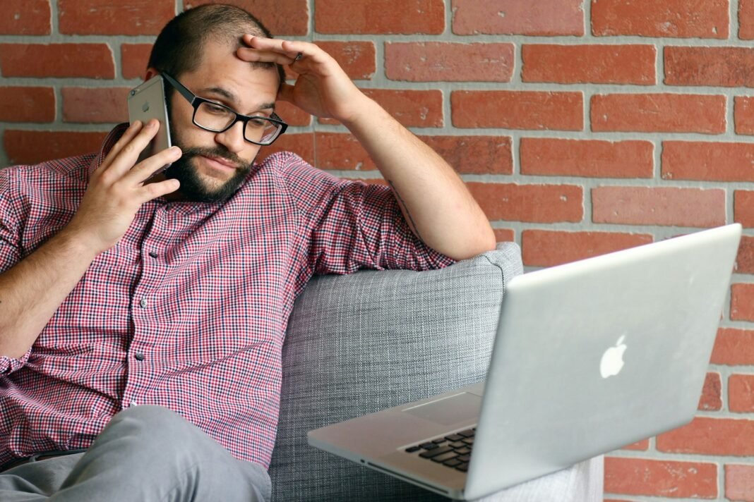 AI May Be Saving You Time, But Is It Improving Your Work? Young Black man on a phone call with his hand on his head while working on a laptop