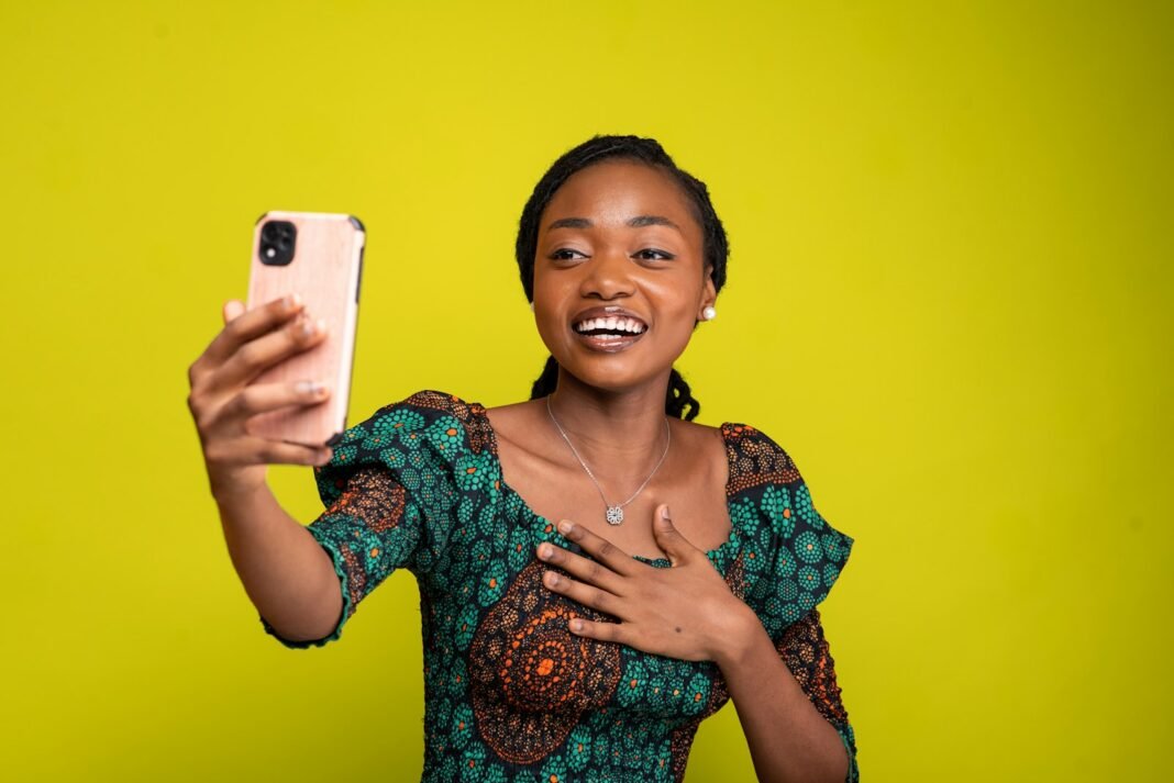 Smiling Nigerian woman in an ankara outfit taking a photo with her phone for her business page