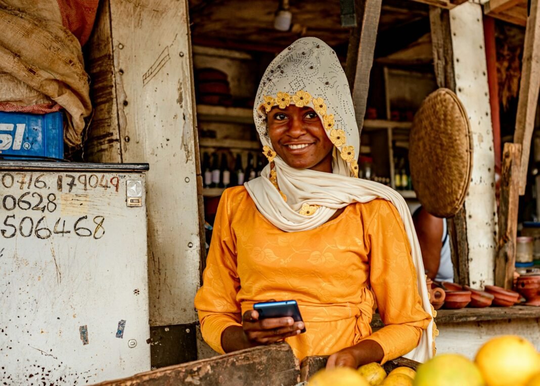 Fake Alerts, Fake Customers: Protect Your Business From Scams Market vendor in front of her fruit stall checking her phone, confirming a customer payment