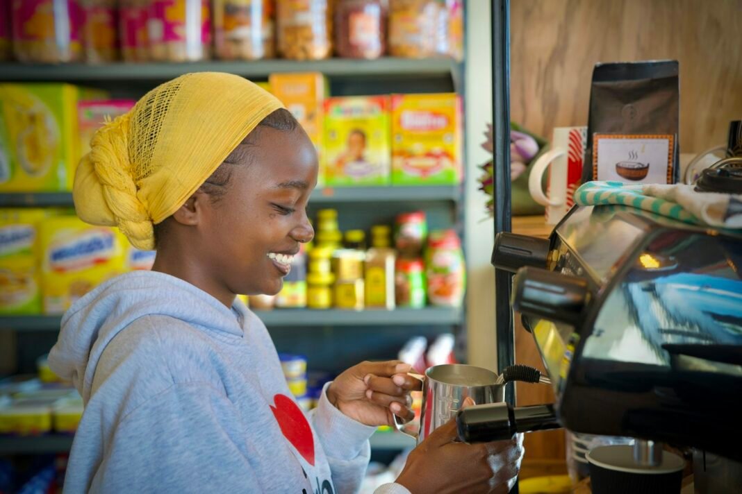 11 Ways Nigerian Small Businesses Can Use AI Without Losing the Human Touch Smiling African woman in a yellow headwrap serving customers behind the counter of her small shop
