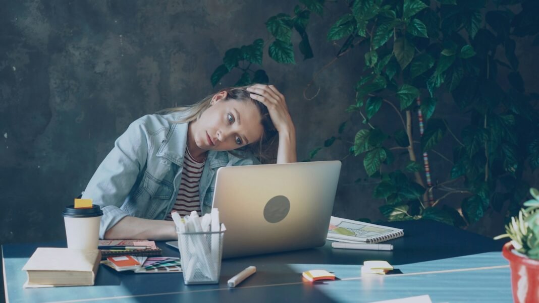 Burnout: Signs, Causes and How to Recover Exhausted worker resting her head on her hand in front of a laptop, a sign of burnout