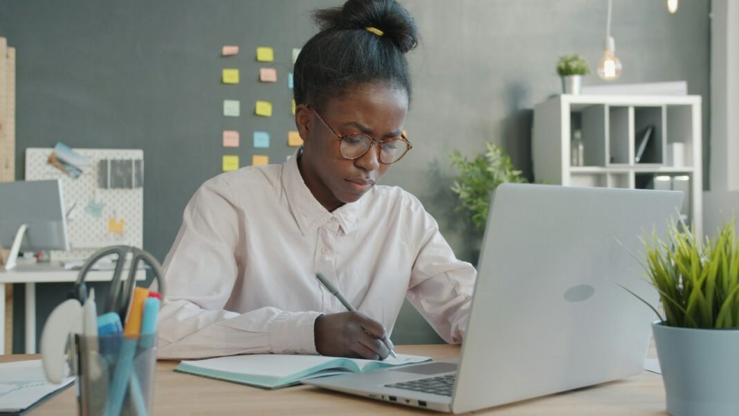 Young Black woman planning her day at a desk with a laptop and notebook