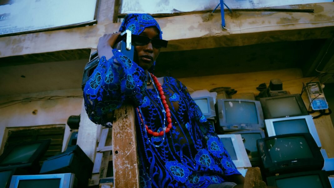 Nigerian man in traditional attire talking on a phone, a reminder to verify urgent calls and voice notes