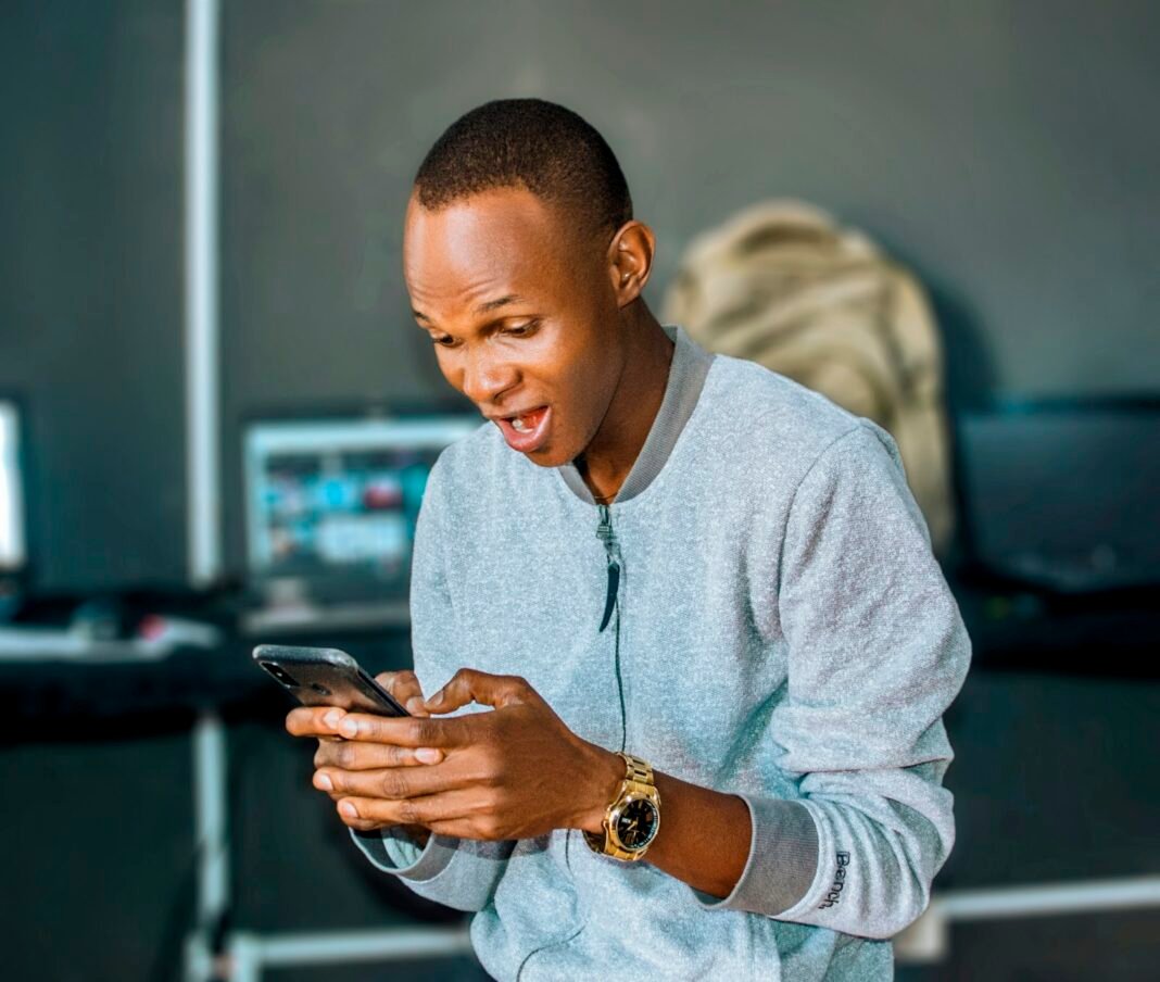 Young Nigerian man reacting to something on his smartphone